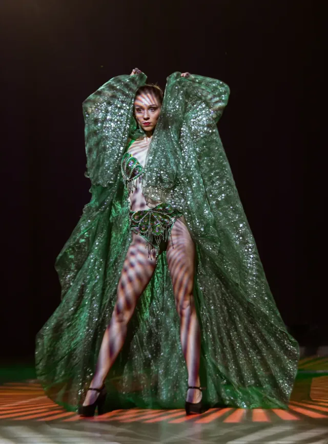 Emerald winged showgirl under striped stage light