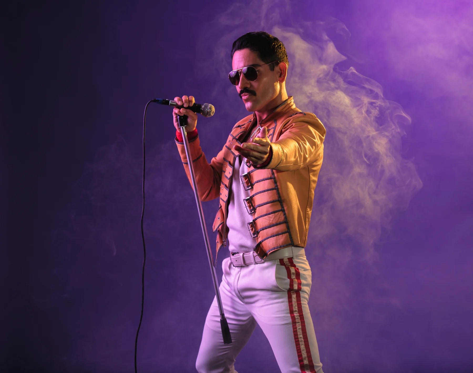 Roy Cruz as Freddie Mercury in the yellow military jacket, singing into a microphone
